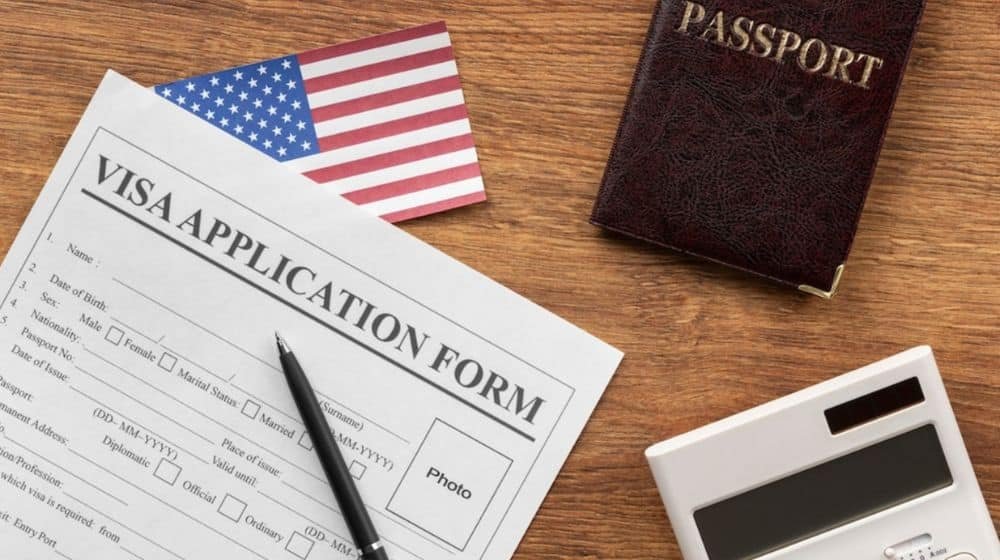 A visa placed in front of the USA flag, illustrating the theme of international travel and the American immigration process.